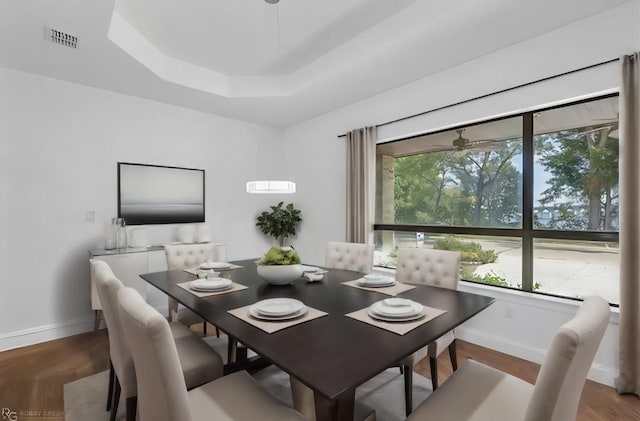dining room featuring a raised ceiling, wood finished floors, visible vents, and baseboards