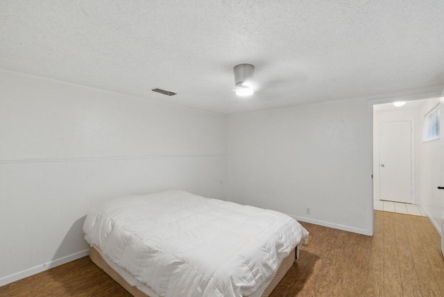 bedroom with ceiling fan, wood finished floors, baseboards, and a textured ceiling