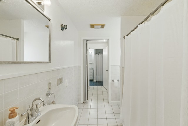 full bath featuring a wainscoted wall, a sink, tile patterned flooring, a textured ceiling, and tile walls