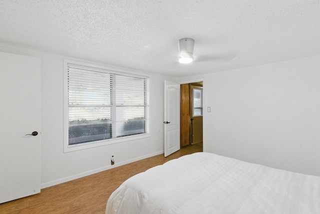 bedroom with a textured ceiling, a ceiling fan, baseboards, and wood finished floors