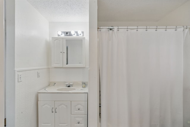 bathroom with vanity, a shower with shower curtain, a textured ceiling, wainscoting, and tile walls