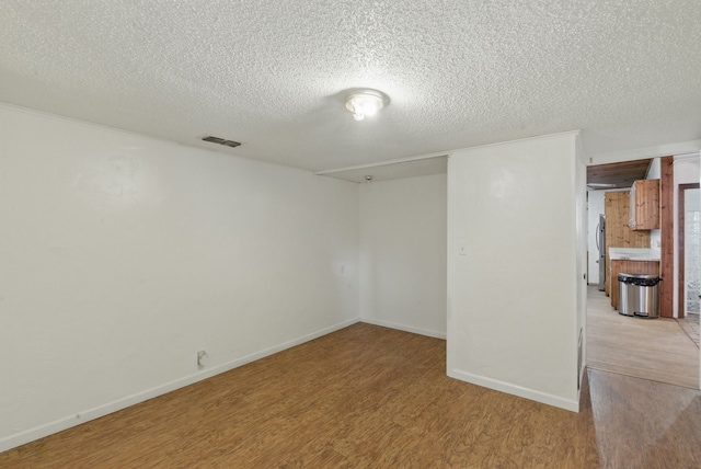 spare room featuring light wood finished floors, visible vents, a textured ceiling, and baseboards