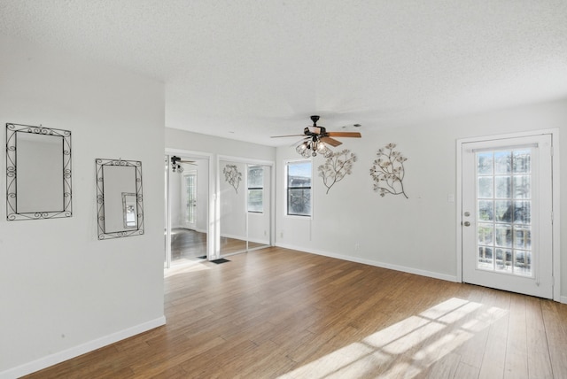 unfurnished living room featuring a textured ceiling, wood finished floors, a ceiling fan, and a healthy amount of sunlight