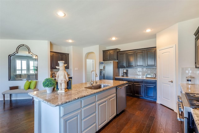 108 Oakmont Dr, Argyle, TX 76226 - kitchen featuring dark wood-type flooring, a sink, stainless steel appliances, arched walkways, and light stone countertops