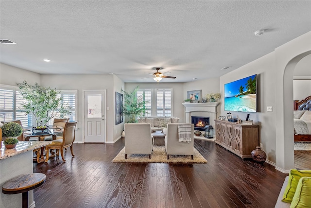 108 Oakmont Dr, Argyle, TX 76226 - living room with visible vents, ceiling fan, a warm lit fireplace, arched walkways, and dark wood-style floors
