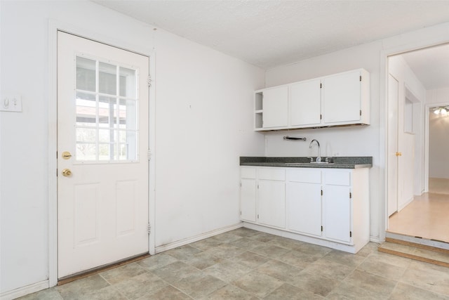 kitchen featuring open shelves, white cabinets, a sink, dark countertops, and baseboards