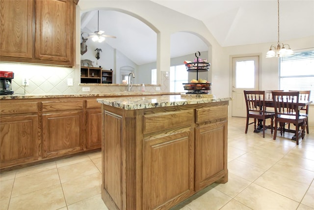 kitchen with a center island, tasteful backsplash, lofted ceiling, light stone counters, and brown cabinetry