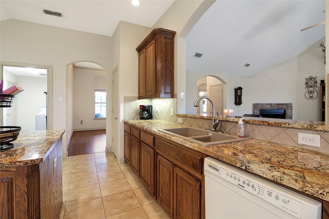 kitchen with vaulted ceiling, white dishwasher, a sink, a fireplace, and visible vents