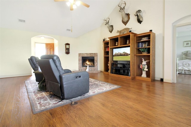 living area featuring wood finished floors, ceiling fan, arched walkways, a premium fireplace, and visible vents