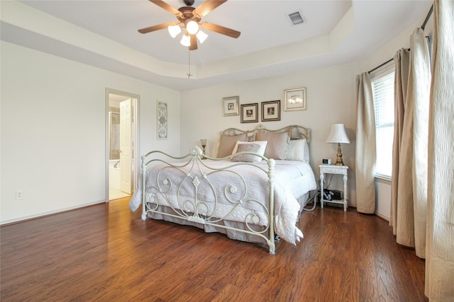 bedroom featuring a tray ceiling, ensuite bathroom, visible vents, a ceiling fan, and wood finished floors