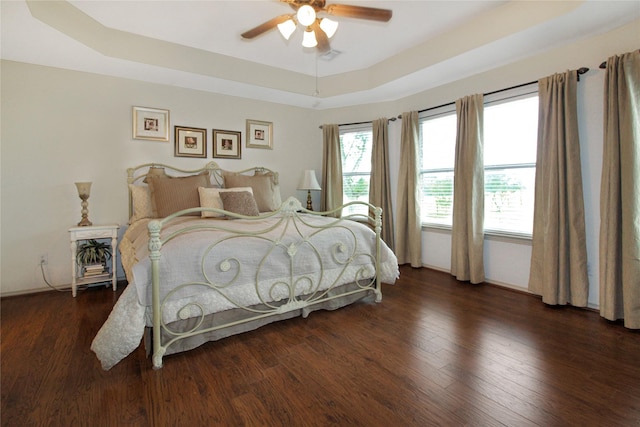 bedroom featuring a tray ceiling, wood finished floors, visible vents, and ceiling fan