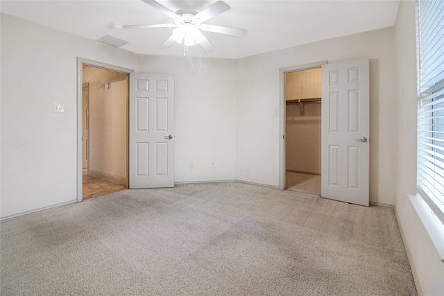 unfurnished bedroom featuring a walk in closet, a ceiling fan, baseboards, and light carpet