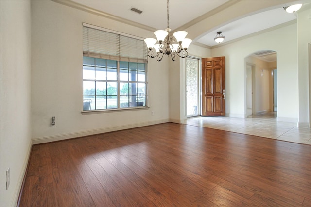 spare room with arched walkways, light wood finished floors, baseboards, a notable chandelier, and visible vents