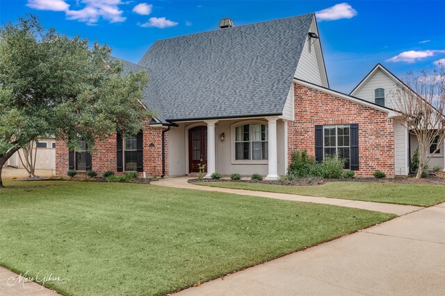 view of front of home with a shingled roof, a front lawn, and brick siding