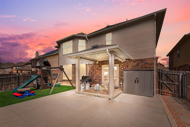 2224 Loreto Dr, Fort Worth, TX 76177 - back of property at dusk featuring a gate, brick siding, a patio, a fenced backyard, and a playground