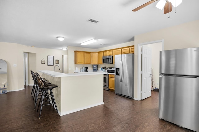 kitchen with a breakfast bar area, ceiling fan, stainless steel appliances, and dark wood-style floors