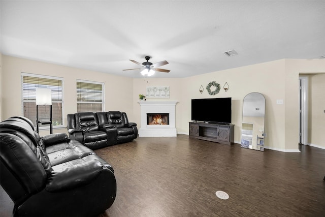 living room featuring a ceiling fan, baseboards, wood finished floors, and a warm lit fireplace