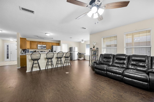living room featuring dark wood-style floors, visible vents, and a ceiling fan