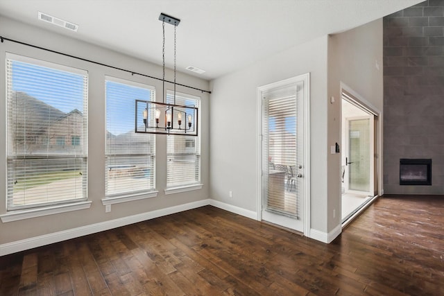 unfurnished dining area with dark wood-type flooring, a chandelier, baseboards, and a fireplace
