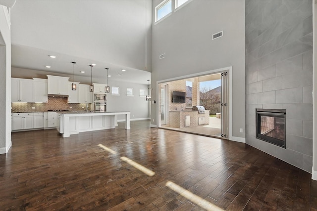 unfurnished living room with dark wood-type flooring, a high ceiling, a tile fireplace, baseboards, and a sink