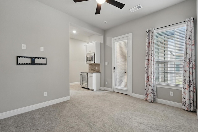 empty room featuring a ceiling fan, light colored carpet, and baseboards