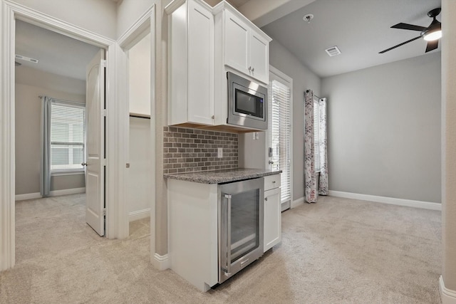 kitchen with stainless steel microwave, beverage cooler, light colored carpet, white cabinetry, and a ceiling fan