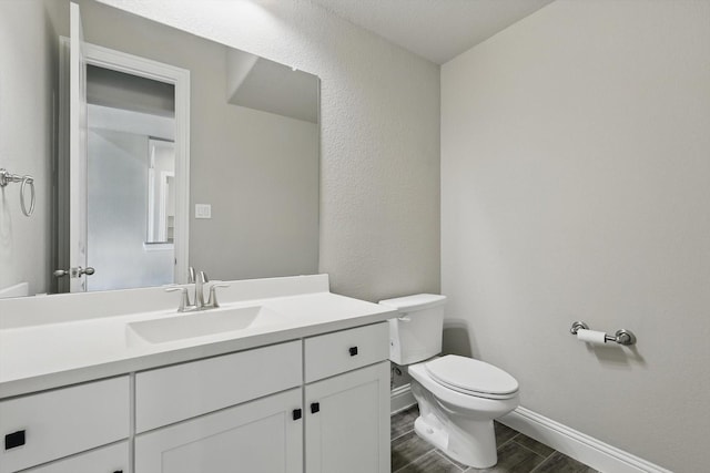 bathroom featuring toilet, wood tiled floors, baseboards, and vanity