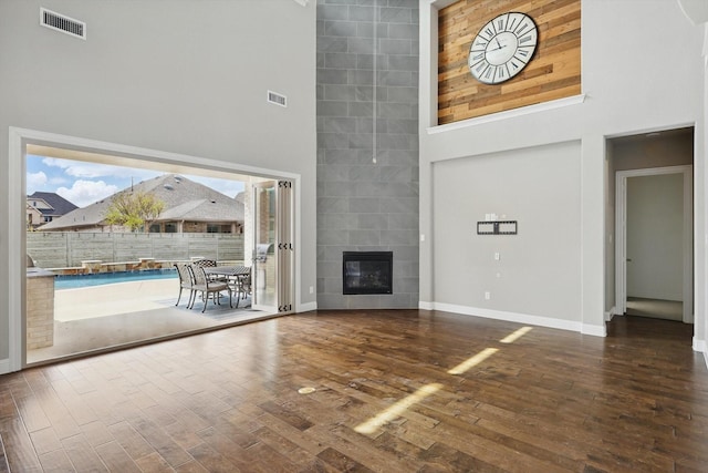 unfurnished living room with a towering ceiling, baseboards, wood finished floors, and a tile fireplace