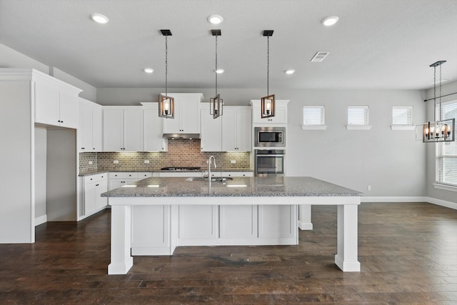 kitchen with stainless steel appliances, a sink, dark wood-style flooring, dark stone counters, and decorative backsplash