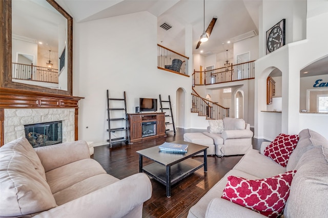 living room featuring high vaulted ceiling, a stone fireplace, arched walkways, wood-type flooring, and visible vents