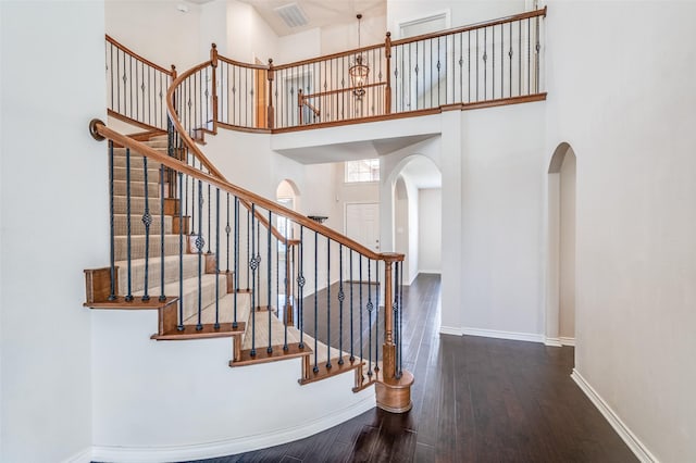 staircase with a towering ceiling, visible vents, arched walkways, baseboards, and hardwood / wood-style flooring