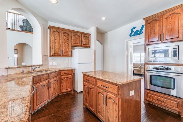 kitchen with a sink, arched walkways, appliances with stainless steel finishes, and light stone counters