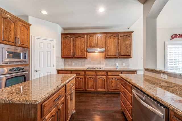 kitchen with light stone counters, brown cabinetry, appliances with stainless steel finishes, and dark wood-style flooring