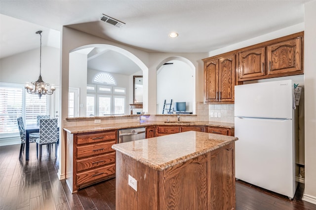 kitchen with brown cabinetry, freestanding refrigerator, light stone countertops, visible vents, and a kitchen island
