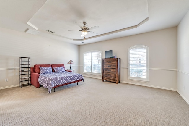 carpeted bedroom featuring ceiling fan, baseboards, a tray ceiling, and visible vents