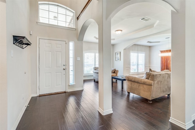 foyer featuring baseboards, visible vents, arched walkways, and dark wood-type flooring