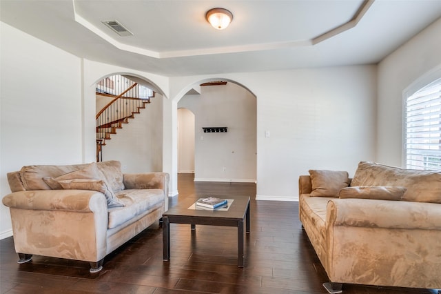 living area featuring arched walkways, dark wood-type flooring, visible vents, and a raised ceiling