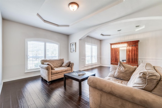 living room with dark wood-style floors, arched walkways, baseboards, visible vents, and a raised ceiling