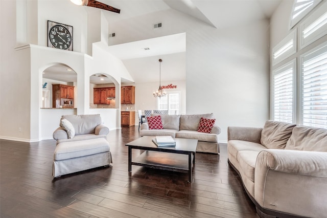 living area with high vaulted ceiling, a notable chandelier, dark wood-type flooring, and visible vents
