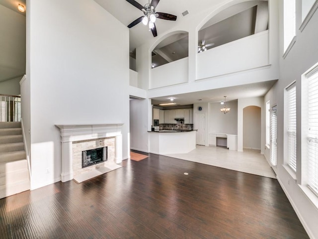 8317 Spring Valley Ln, Plano, TX 75025 - unfurnished living room featuring a tiled fireplace, ceiling fan, stairway, light wood finished floors, and a towering ceiling