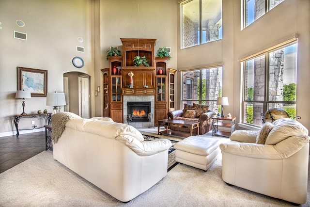 living room with a towering ceiling, plenty of natural light, arched walkways, a tile fireplace, and baseboards