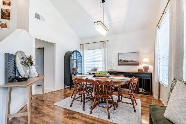 dining room with wood finished floors, visible vents, high vaulted ceiling, and baseboards