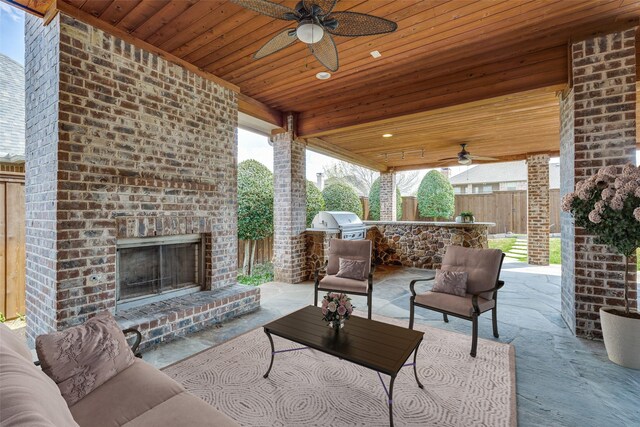 view of patio / terrace with grilling area, a ceiling fan, an outdoor living space with a fireplace, a fenced backyard, and an outdoor kitchen