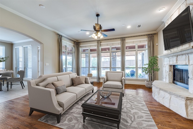 living area with a fireplace, arched walkways, a ceiling fan, visible vents, and ornamental molding