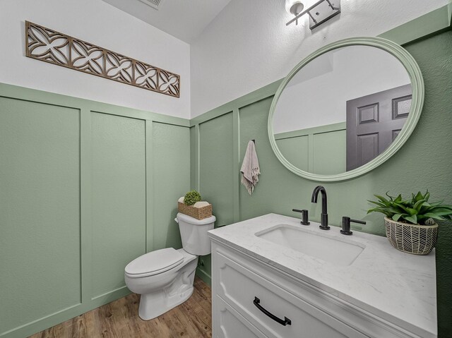 bathroom featuring toilet, vanity, a decorative wall, and wood finished floors