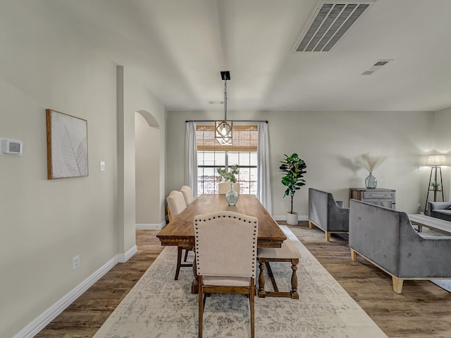 dining room featuring wood finished floors, visible vents, baseboards, and arched walkways