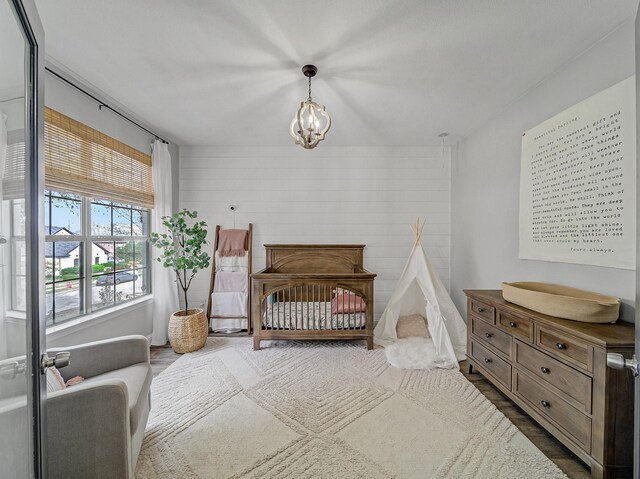 bedroom with wood finished floors, an inviting chandelier, and a nursery area