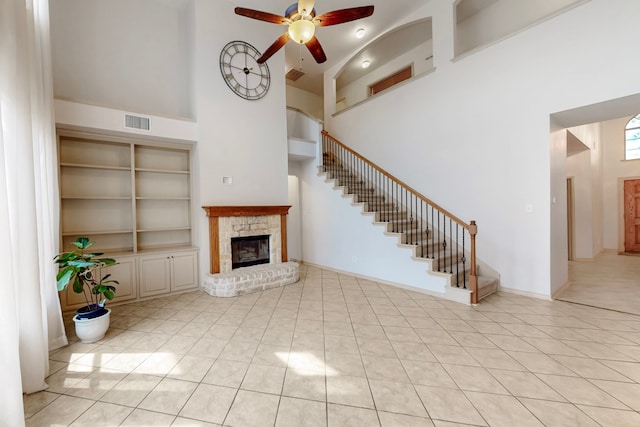 1312 Cattle Crossing Dr, Fort Worth, TX 76131 - unfurnished living room featuring a fireplace with raised hearth, a towering ceiling, ceiling fan, stairs, and light tile patterned floors