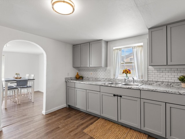 5536 Goodman Ave, Fort Worth, TX 76107 - kitchen with gray cabinetry, a sink, arched walkways, backsplash, and light wood-type flooring