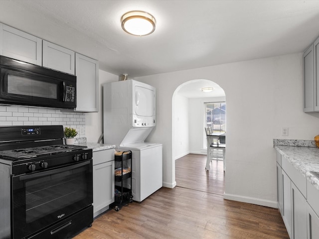5536 Goodman Ave, Fort Worth, TX 76107 - kitchen featuring black appliances, estacked washer and dryer, arched walkways, baseboards, and light wood-type flooring